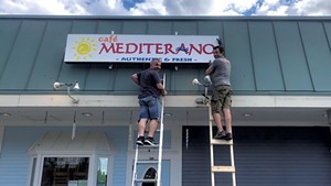 Cafe Mediterano owner Barney Crnalic (left) and friend, Mehmed Tuco, hang the sign at the new location.