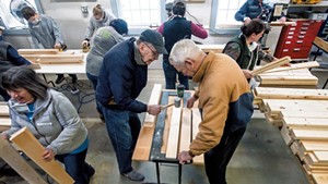 Volunteers use a mallet to make holes in wood that will eventually become a bed