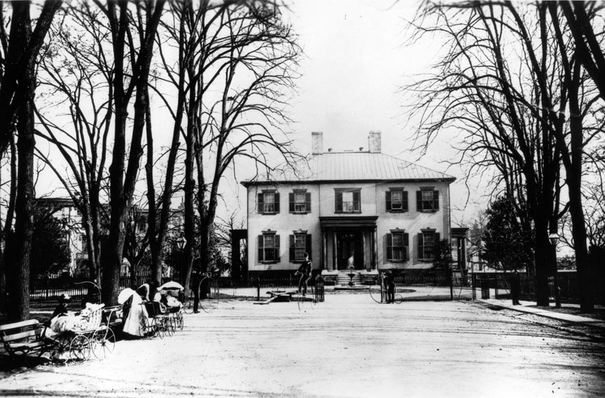 In this 1880s photograph the Executive Mansion serves as a backdrop for Capitol Square outings, including tending baby carriages and riding high-wheel bicycles when the neighborhood remained partially residential.