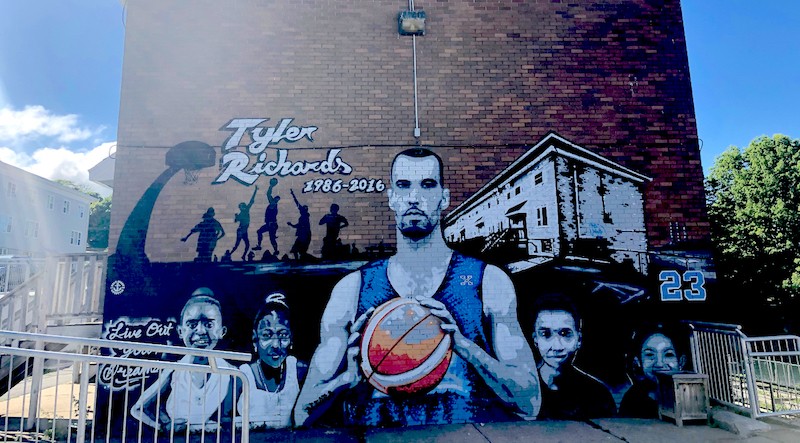 In the mural painted in his honour, Tyler Richards looks out over his community with a pensive, protective glare.