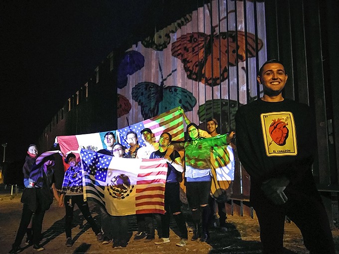 High school students from Tucson posing by art projected on the U.S.-Mexico border in Nogales, Arizona.