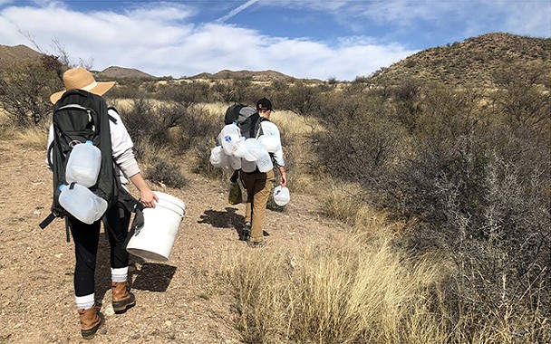 Volunteers Greena Jackson and Justine Orlovsky-Schnitzler carry empty water jugs from a supply drop site. The Jugs, which were dropped at the site two weeks earlier, appear to be slashed and emptied. - NICOLE LUDDEN