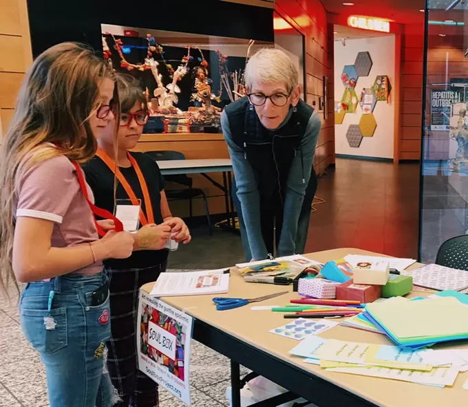 Meg Pradelt with the Soul Box Project shows two young girls how to make the origami style boxes at the Joel D. Valdez Main Library on Jan. 8. - AUSTIN COUNTS