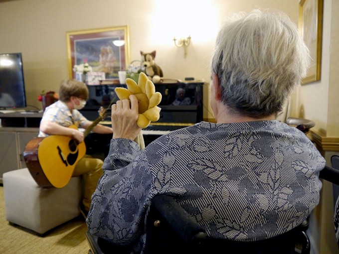 Pat Rush holds “Sunny” as she listens to memory care coordinator Taylor Johnson tune his guitar before a musical session with residents at Sunrise, a Pennsylvania retirement community where Rush was in the memory care wing. - FILE PHOTO BY EMILY SCHMIDT/CRONKITE NEWS